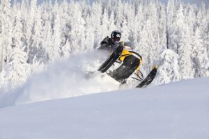Snowmobile splashing snow with snowy pines in the background
